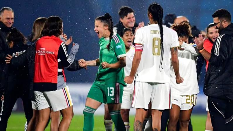 Grupo de jogadoras e comissão técnica comemorando em campo, sob uma leve chuva.