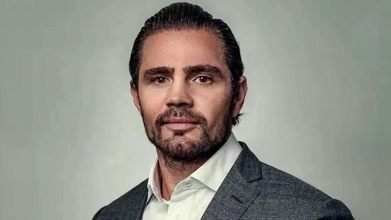 Foto colorida de tronco de homem pardo e com barba. Ele usa uma blusa branca e um blazer cinza - Metrópoles