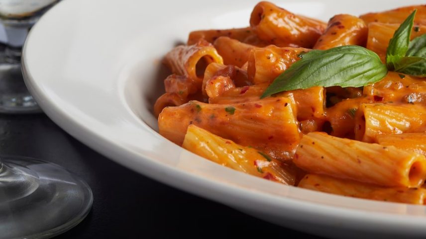 Rigatoni alla vodca num prato branco ao lado de uma taça de vidro. Foto: Alene Pierro/ Adobe Stock