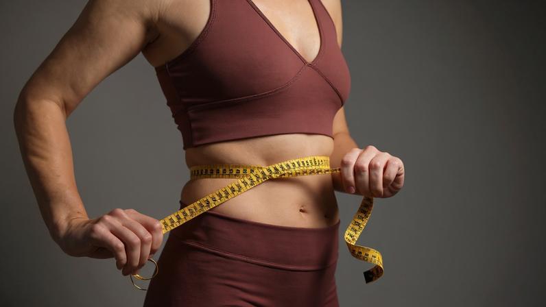 Foto colorida de mulher com fita métrica na barriga. Ela usa um cropped e uma legging - Metrópoles - emagrecer