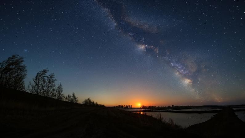 An arched band of the Milky Way bends across a twilight sky.