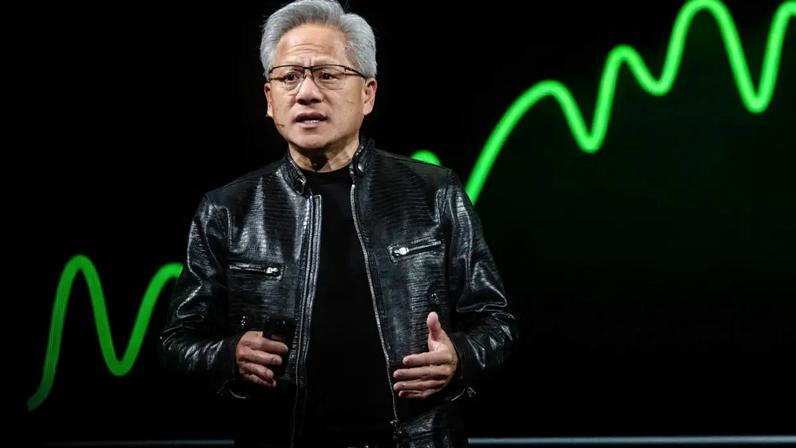 Jensen Huang, da Nvidia, homem asiático de cabelos grisalhos e óculos, vestindo jaqueta de couro preta, gesticula enquanto fala em um palco escuro com um gráfico de linha verde neon ao fundo