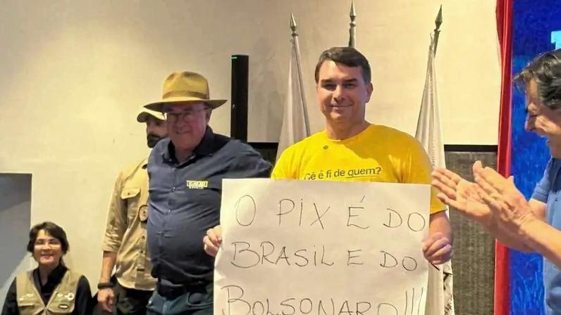 Flávio Bolsonaro (PL-RJ) levanta cartaz escrito "o Pix é do Brasil e do Bolsonaro", em Contagem, Minas Gerais. Foto: reprodução / rede x