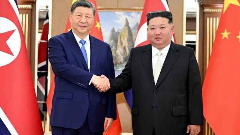 Na imagem, Xi (à esq.) e Kim Jong-un (à dir.) se cumprimentam com bandeiras de ambos os países ao fundo
