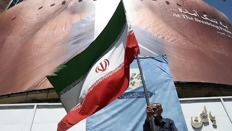 Homem segura bandeira iraniana perto de outdoor anti-EUA representando o presidente dos EUA, Donald Trump, e o Estreito de Ormuz, em Teerã, Irã, em 30 de maio de 2026