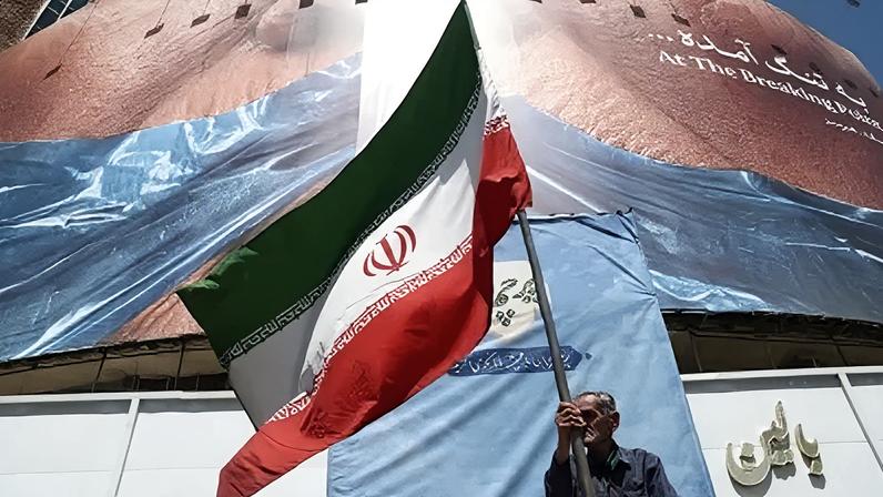 Homem segura bandeira iraniana perto de outdoor anti-EUA representando o presidente dos EUA, Donald Trump, e o Estreito de Ormuz, em Teerã, Irã, em 30 de maio de 2026