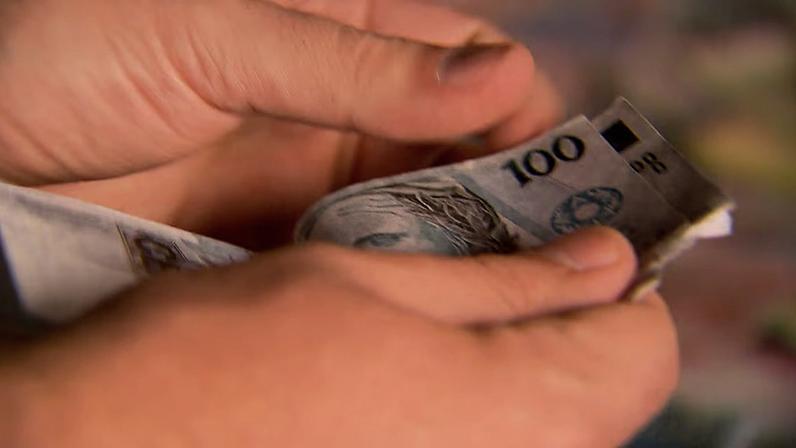 Duas mãos folheiam notas de R$100, contando quanto consta no bolo de dinheiro.