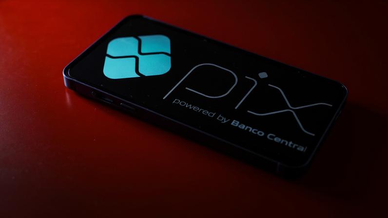 Imagem colorida mão com dinheiro e aplicativo PIx dinheiro pagamento moeda digital - Metrópoles