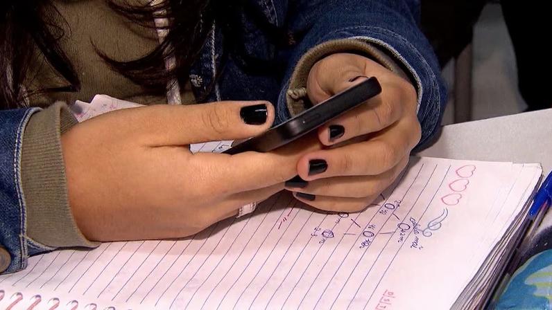 Mãos segurando um celular sobre um caderno com anotações