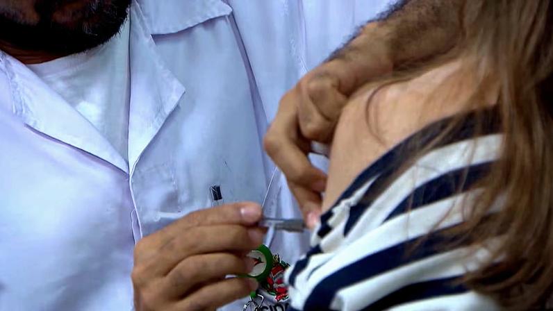 Homem aplica vacina em braço de mulher
