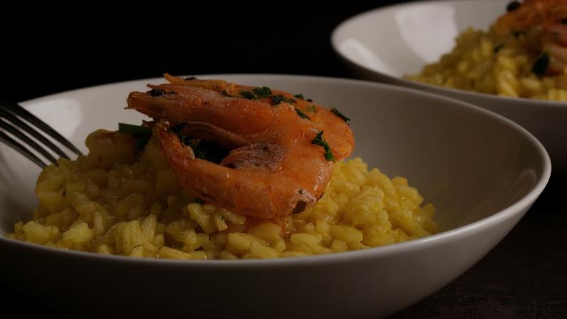Risoto de camarão com açafrão, decorado com salsinha e servido em prato fundo. Foto: Olga - stock.adobe.com