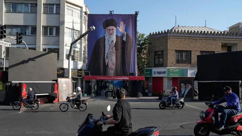 Motocicletas passam perto da residência onde o líder supremo iraniano, aiatolá Ali Khamenei, retratado em um painel, foi morto em ataques dos EUA e de Israel em 28 de fevereiro, em Teerã