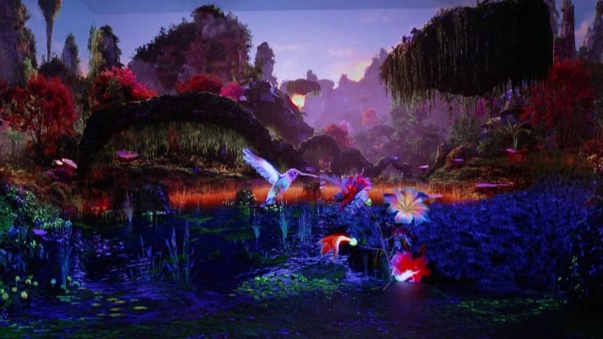Paisagem repleta de vegetação luminosa em tons de azul, roxo, vermelho e rosa. No centro, um beija‑flor brilhante flutua sobre flores que parecem emitir luz, que reflete nas águas de um lago cintilante.