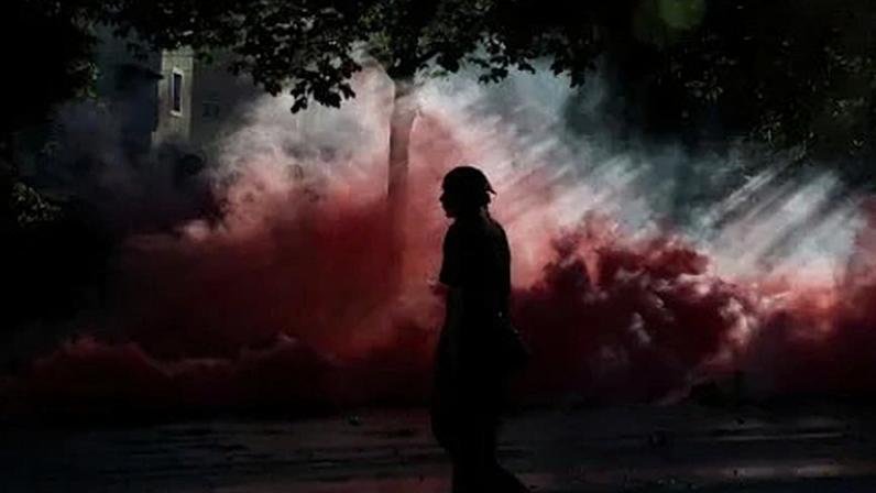 Pessoa caminha em meio a nuvens de fumaça durante protesto em Genebra contra a próxima cúpula do G7 em 14 de junho de 2026