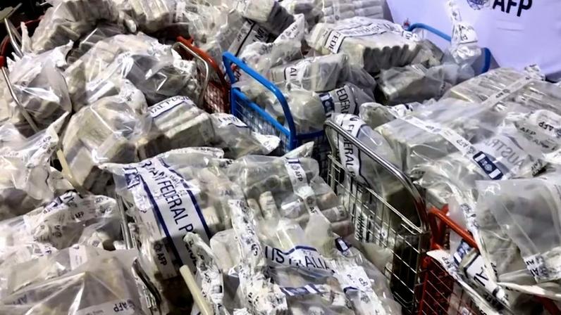 Pacotes lacrados empilhados em carrinhos e no chão durante grande apreensão de drogas