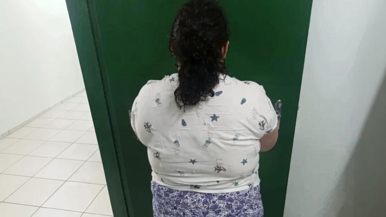 Mulher de costas, com cabelo escuro preso, vestindo camiseta branca estampada com estrelas e shorts florido, em frente a uma porta verde