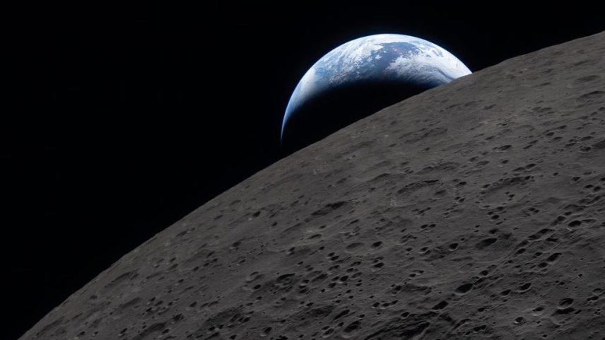 A Terra azul e branca surge no horizonte lunar, que mostra sua superfície cinza escura e crateras em primeiro plano, contra o espaço preto.