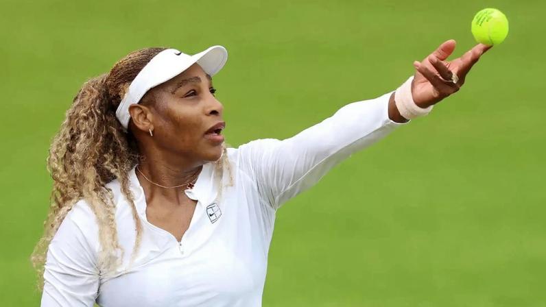 Serena Williams throws a tennis ball in the air to hit a serve.
