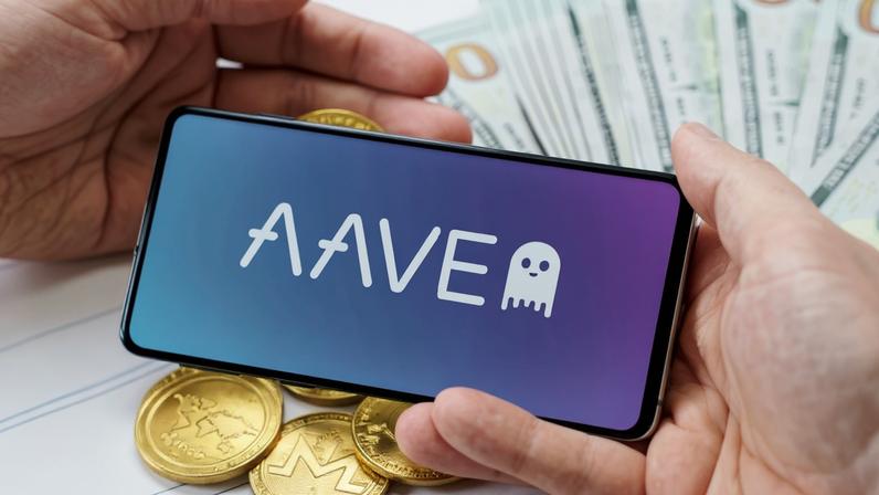 Uma mão segunra smartphone comlogomarca Aave e outra mãos critpomeodas Ethereum