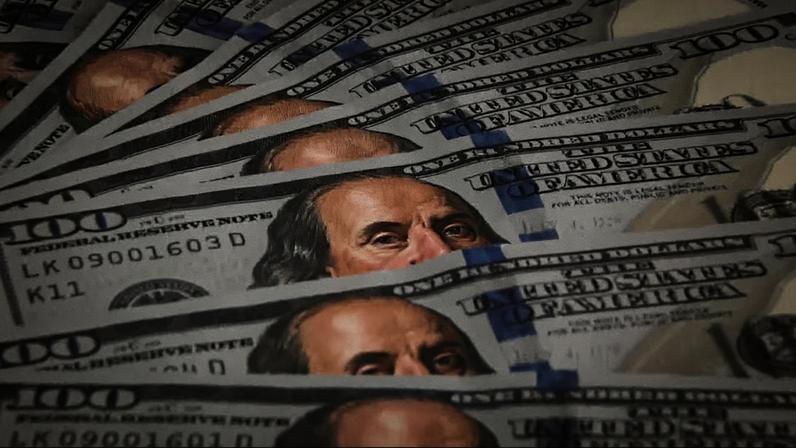 Várias notas de 100 dólares americanos espalhadas em leque, destacando detalhes das cédulas