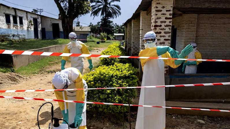 Profissionais de saúde usando equipamentos de proteção atravessam para uma área restrita ao lado de uma unidade de isolamento do Hospital Geral de Referência de Mongbwalu, em Mongbwalu, na República Democrática do Congo, em 26 de maio de 2026. (Foto: Michel Lunanga)
