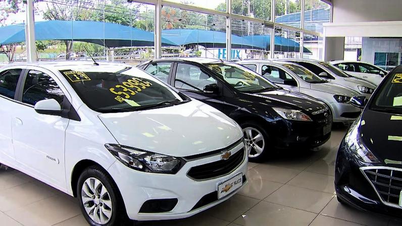 Carros seminovos expostos em concessionária, alinhados em um showroom iluminado com etiquetas de preço nos para-brisas
