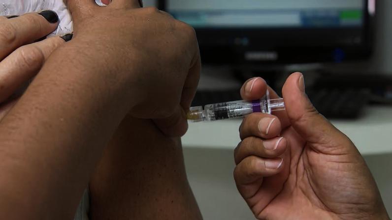 Profissional de saúde aplica vacina no braço de uma pessoa durante atendimento em unidade de saúde