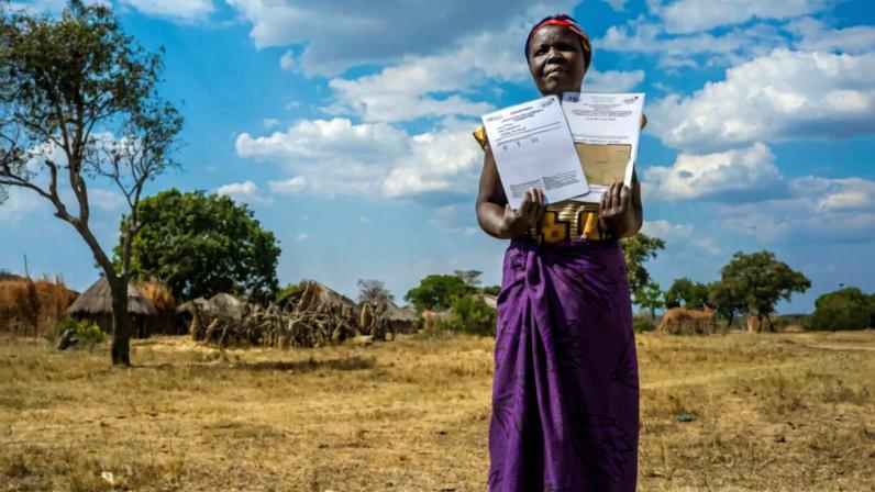A woman holds up land tenure certificates in Chipata, Zambia (2017). Image by USAID via Flickr (CC BY-NC-SA 2.0)
