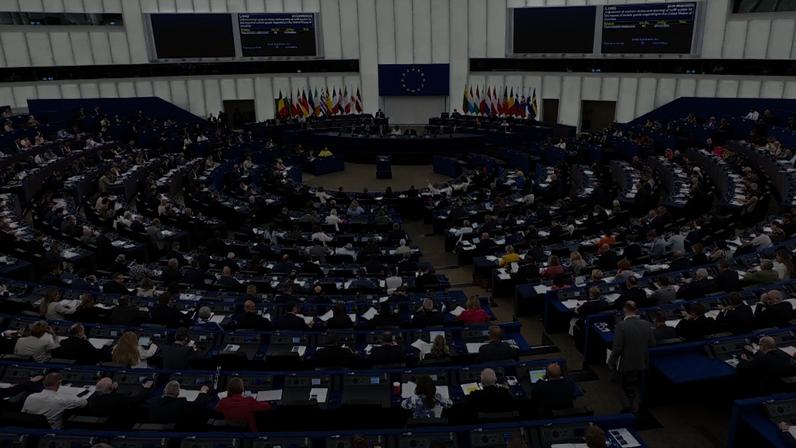 Vista ampla de plenário do Parlamento Europeu, com muitas pessoas sentadas em formato semicircular e bandeiras ao fundo