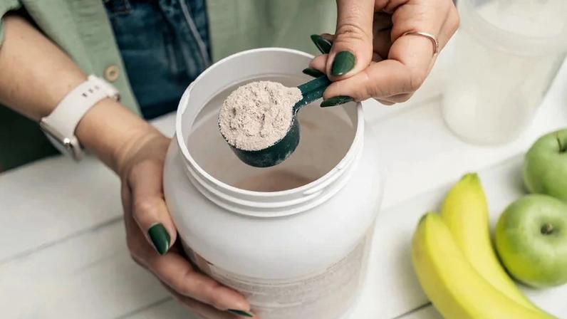 Close-up das mãos de uma mulher retirando whey protein de um pote. Metrópoles