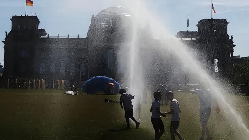 People pass by a watering system in front of the Reichstag on a hot summer day on June 24, 2026