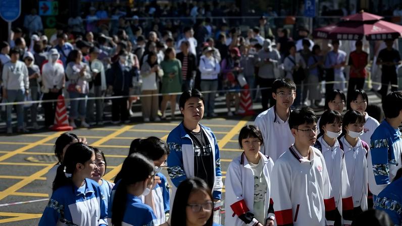 Pais (ao fundo) aguardam do lado de fora de uma escola enquanto alunos fazem fila para entrar no primeiro dia do Exame Nacional de Admissão ao Ensino Superior da China (NCEE), conhecido como "gaokao", em Pequim — Foto: WANG ZHAO/AFP