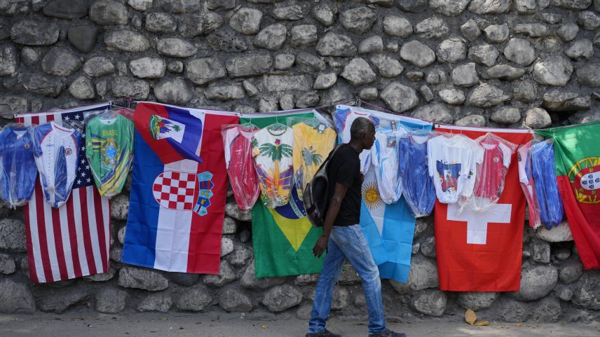 Um pedestre caminha ao lado de bandeiras e camisas de futebol à venda em uma rua de Porto Príncipe, Haiti — Foto: AP Photo/Odelyn Joseph