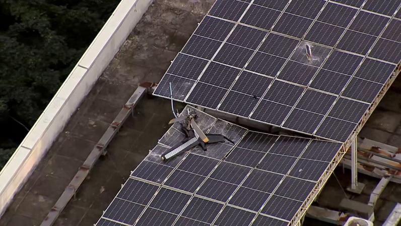 Resto de um rotor de calda ficou em cima de painéis solares de um edifício ao lado do local da queda — Foto: Reprodução/TV Globo