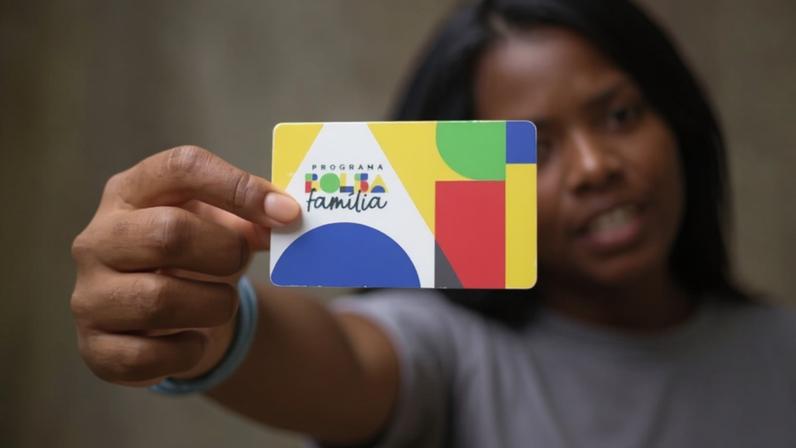 Programa paga ao menos R$ 600 por família e inclui adicionais de R$ 50 ou R$ 150; na imagem, uma mulher segura cartão do Bolsa Família