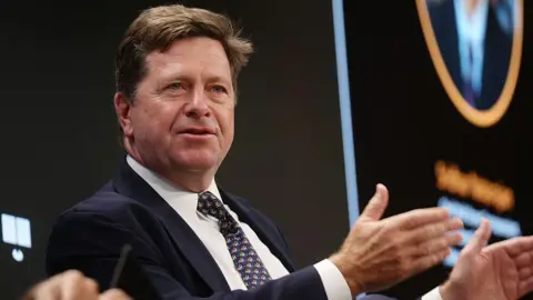 Getty Images Jay Clayton wearing a suit and raising his hands as he speaks at an event