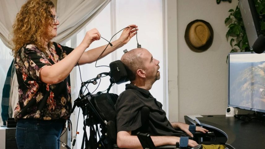 Imagem mostra uma mulher esticando fios ligados à cabeça de um homem em cadeira de rodas - Metrópoles