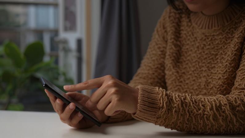 Imagem mostra uma mulher de casaco marrom mexendo no celular com um dedo - Metrópoles