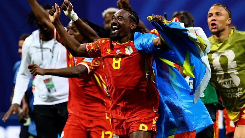DR Congo's Samuel Moutoussamy celebrates with their national flag after the match as they qualify for the knockout stages of the World Cup