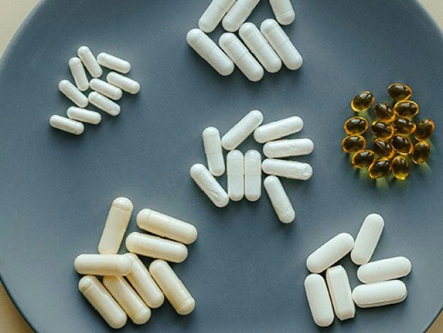 Fotografia de um parto com cápsulas de vitaminas, ao lado garfo e faca.