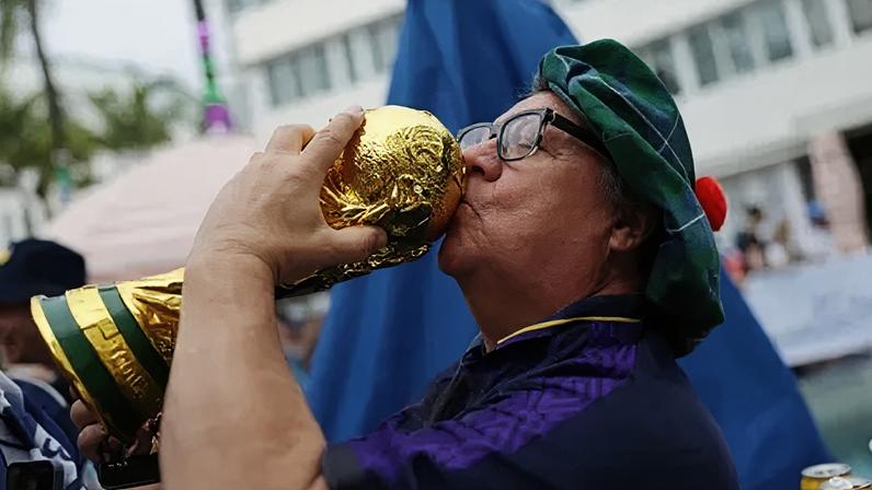 A Scotland fan kisses a model of the World Cup trophy and prays for luck ahead of the Brazil game
