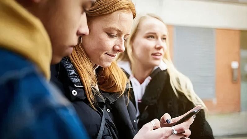 Getty Images Three teenagers standing outside and looking at one phone