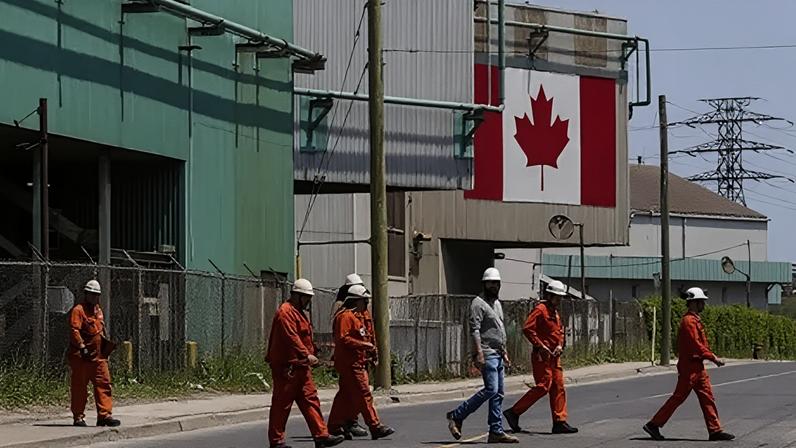 AFP via Getty Images A Canadian national flag is seen in the background as seven workers dressed in orange work suits and white hard hats cross the street in front of ArcelorMittal Dofasco's steel manufacturing buildings in Hamilton, Ontario.