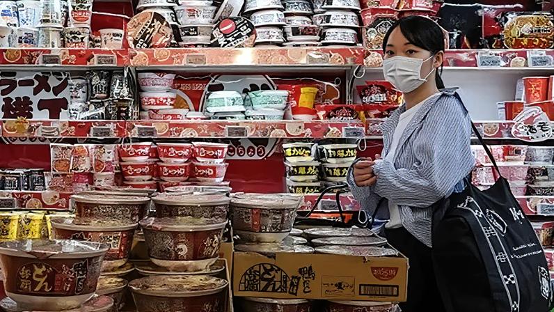 AFP via Getty Images A customer walking past a row of shelves filled to the brim with instant noodles at a supermarket in Japan.