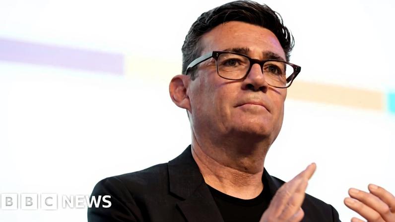 Andy Burnham wearing a black t-shirt and jacket, and black-rimmed glasses