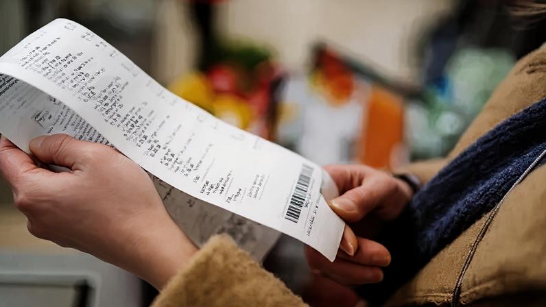 Getty Images Close-up of a woman holding and reviewing a grocery receipt after shopping.