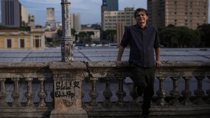 Lô Borges posa para retratato frente a mureta na rua Sapucaí, em Belo Horizonte, e a capa do disco 'A Estrada'