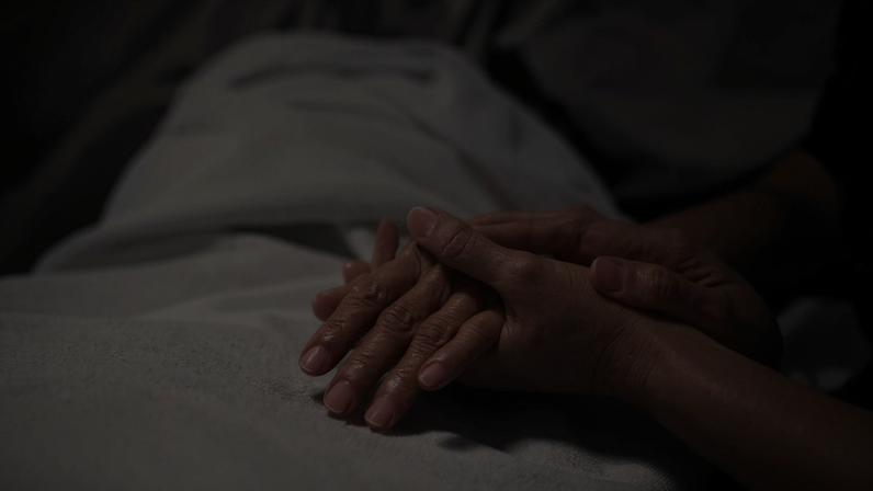 An elderly woman in a hospital bed holding someone's hand.