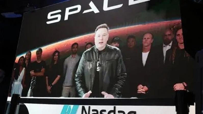 Getty Images Elon Musk stands at a podium with the Nasdaq logo on it wearing a black t shirt and black leather jacket.