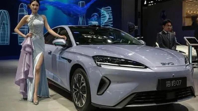Getty Images A woman in a silver evening gown stands next to a grey electric vehicle made by Chinese automaker BYD displayed on media day at the Beijing International Auto Exhibition